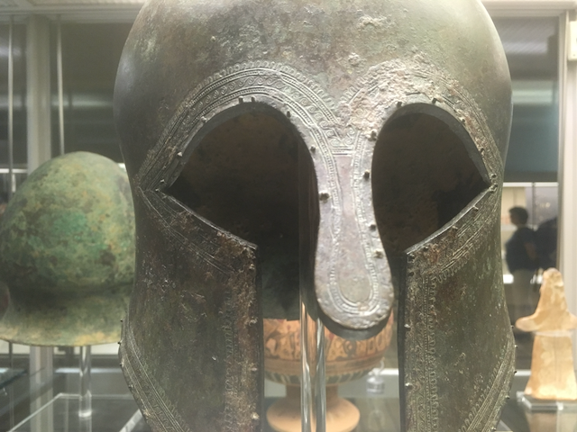 The image shows a Greek warrior's bronze helmet, circa 700 BC (The British Museum, photo by Andrew Sutherland).